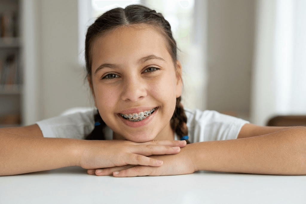 A young girl smiling, wearing braces on the upper teeth