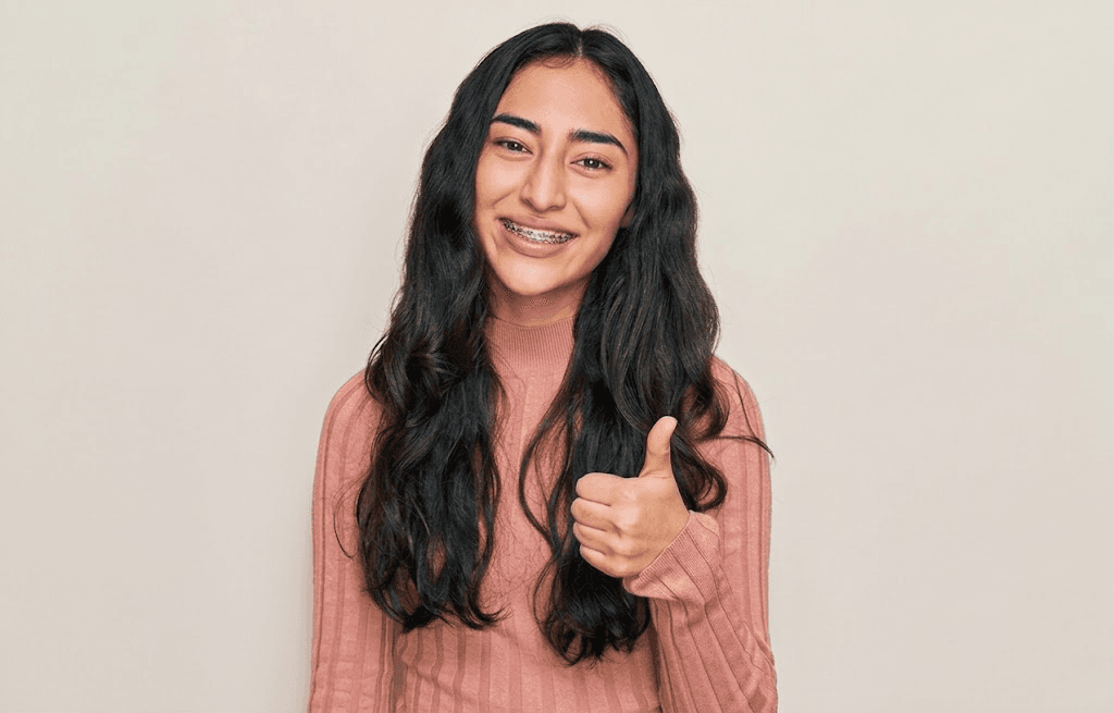 A teenage girl with braces smiling and giving a thumbs up